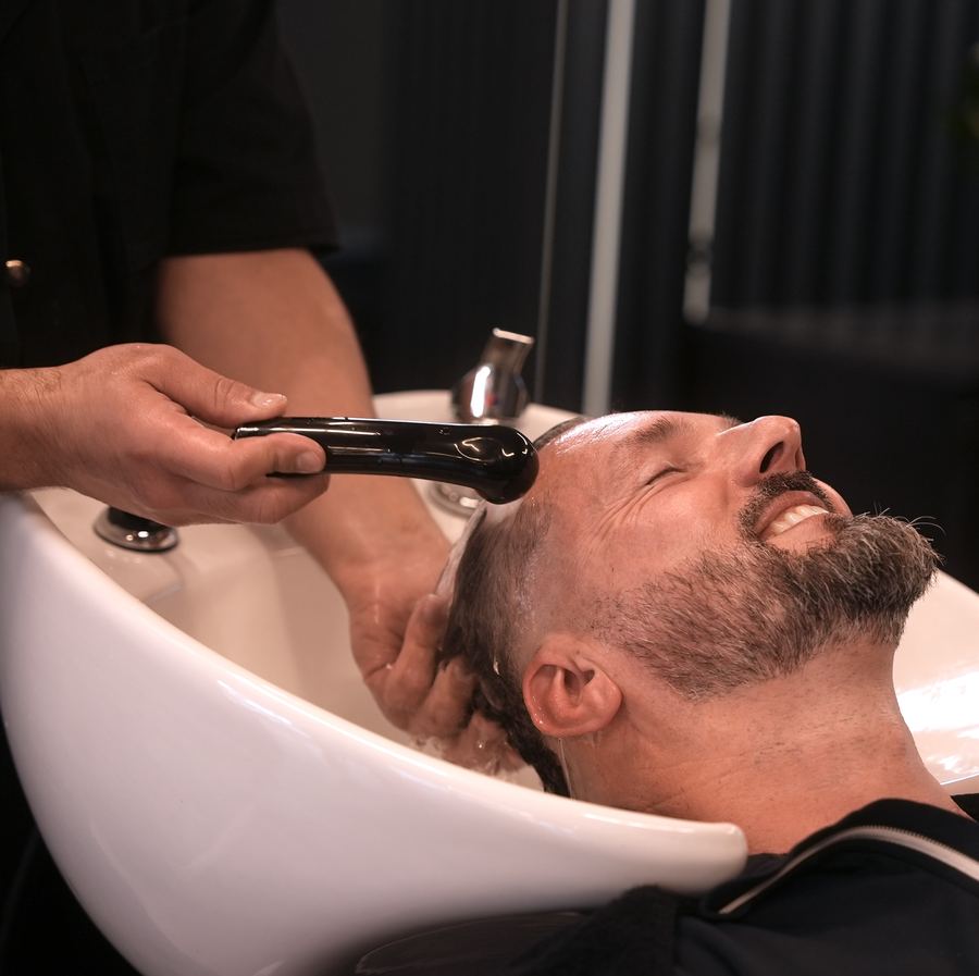 Kunde mit geschlossenen Augen bei der Haarwäsche am Waschbecken