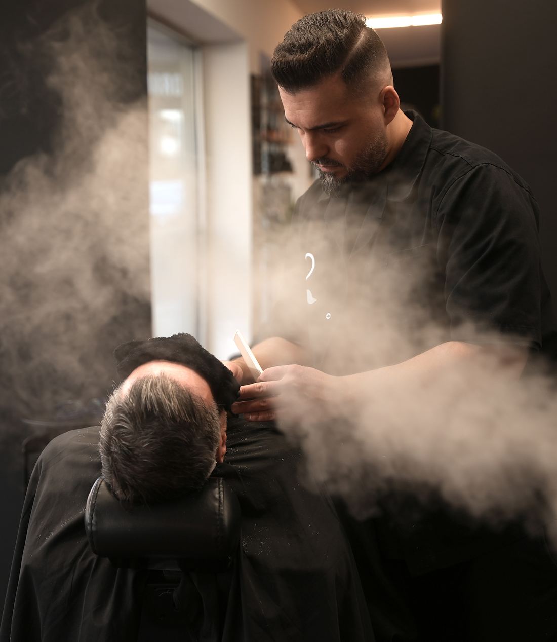 Barbier bei der Nassrasur, Dampf steigt über dem Kunden auf